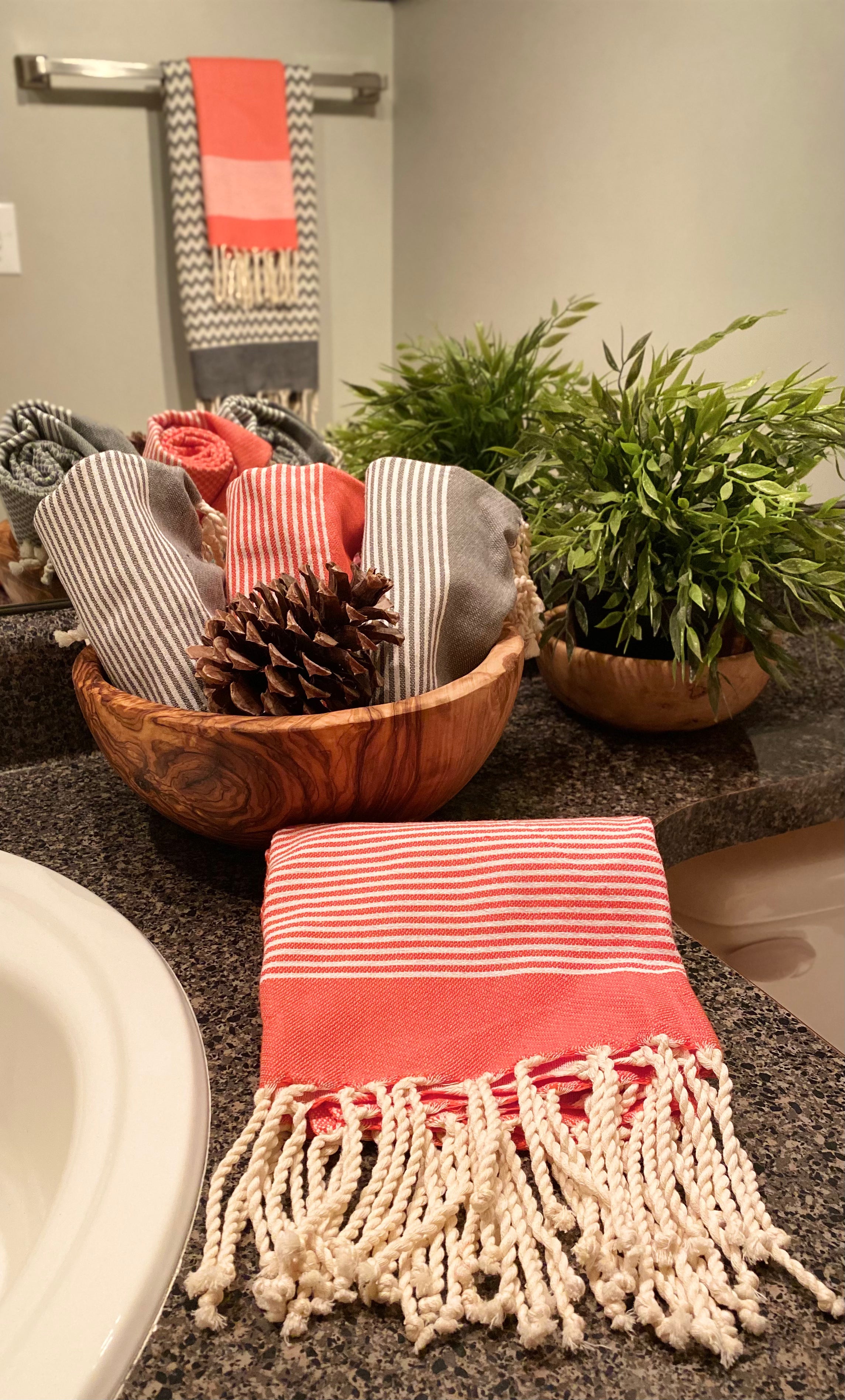 Orange and gray striped Fouta hand towels displayed in decorative olive wood bowl on bathroom counter. Two examples of home goods customers can shop for online.