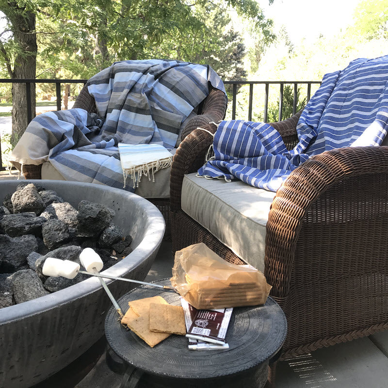 Fouta bath towels wrapped as cozy blankets around chairs at a campfire, ideal warmth and comfort outdoors.