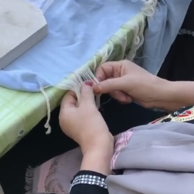 Hands of a Tunisian woman twisting tassel ends of a fouta towel, finishing a piece often chosen as a thoughtful bridal shower gift.