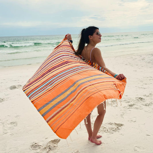 Woman holding Nabeul Sun Tile Golden Hour fouta towel on beach showing full size and striped design