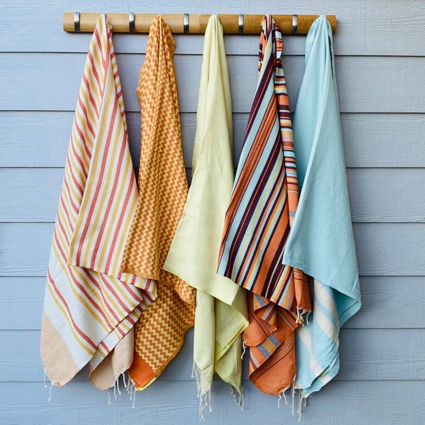 Collection of fouta towels including Nabeul Sun Tile Golden Hour hanging on wall showing color variations