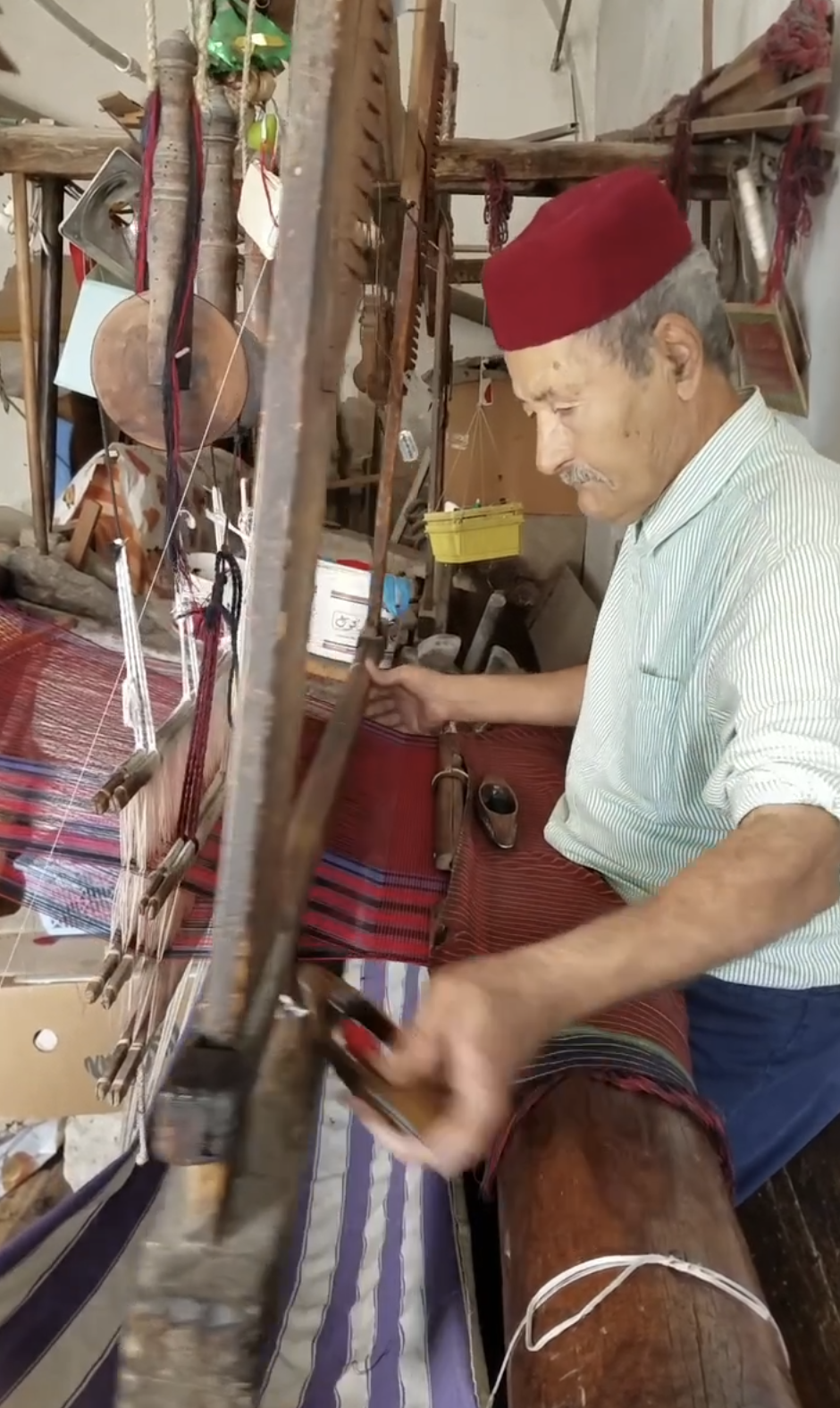 Close-up of a skilled weaver in a red cap guiding a wooden shuttle through a loom, crafting high-quality cotton towels by hand.