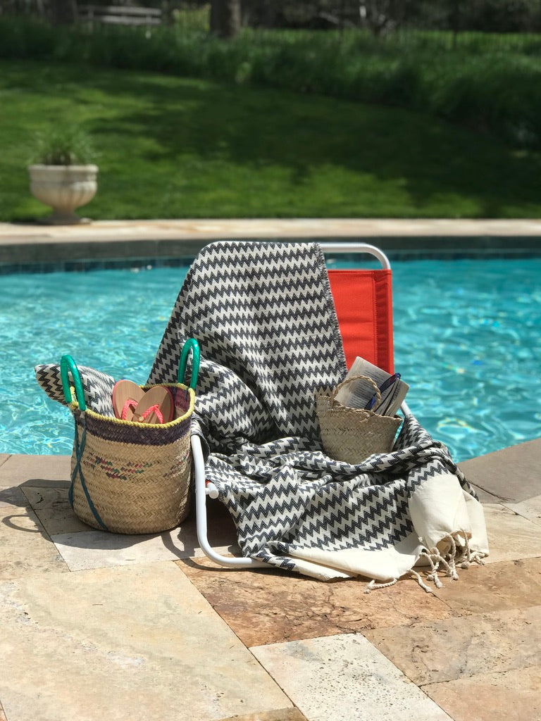 Zig zag patterned fouta draped over a red beach chair by the pool, showcasing stylish beach towels with a summery vibe.