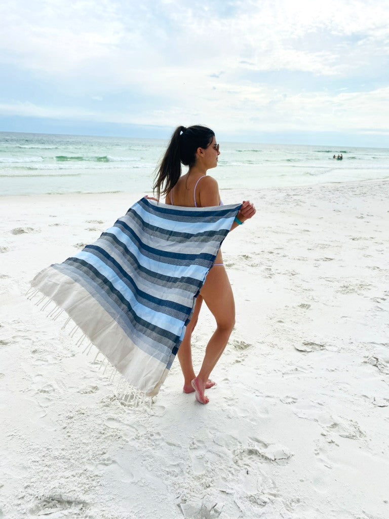 Woman on the beach laying out on one of our oversized fouta beach towels, ready for a relaxing day by the water.