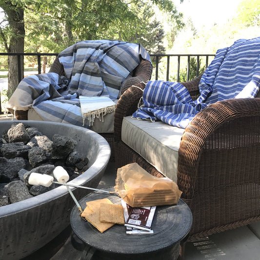 Fouta bath towels wrapped as cozy blankets around chairs at a campfire, ideal warmth and comfort outdoors.