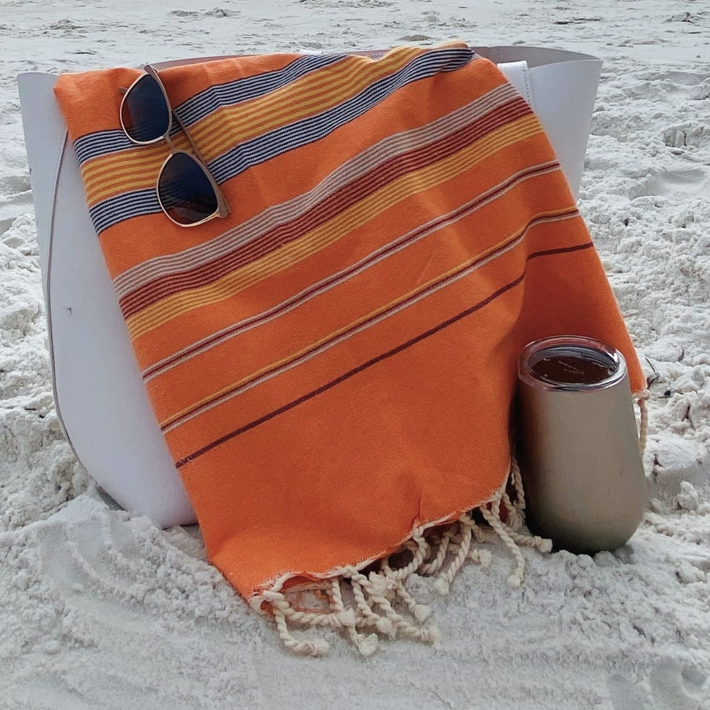 Nabeul Sun Tile Golden Hour fouta towel draped over beach bag with sunglasses and drink on sandy beach