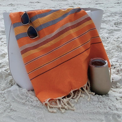 Nabeul Sun Tile Golden Hour fouta towel draped over beach bag with sunglasses and drink on sandy beach