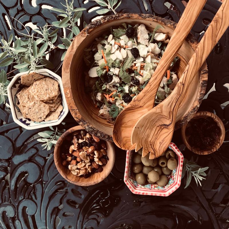 Elegant Mediterranean table spread with olive wood bowls and serving utensils with salads, figs, nuts, and crackers.